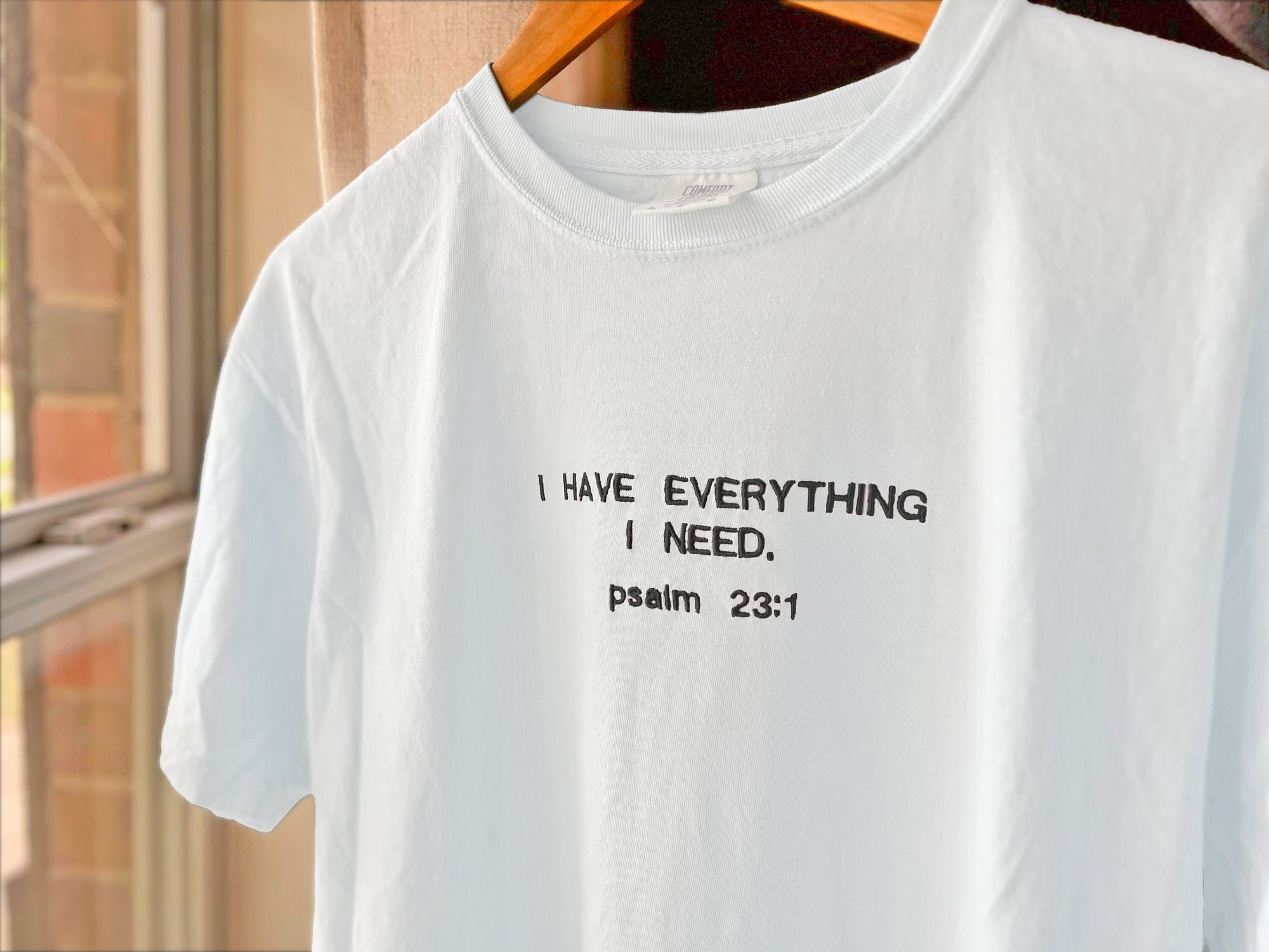 White crewneck t-shirt with the text 'I HAVE EVERYTHING I NEED. psalm 23:1' embroidered in black.