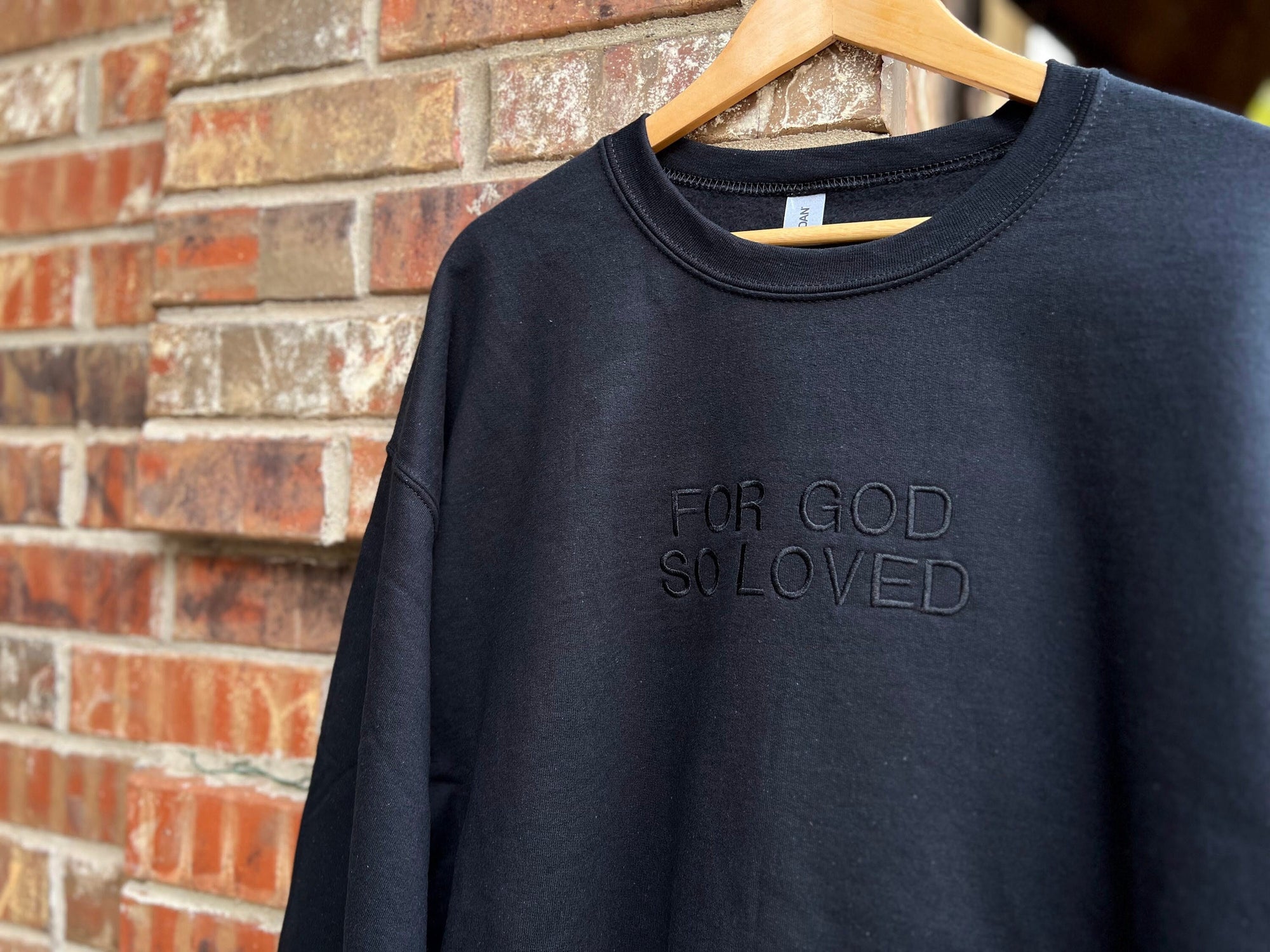Black sweatshirt with the text 'FOR GOD SO LOVED' embroidered on the front in capital letters