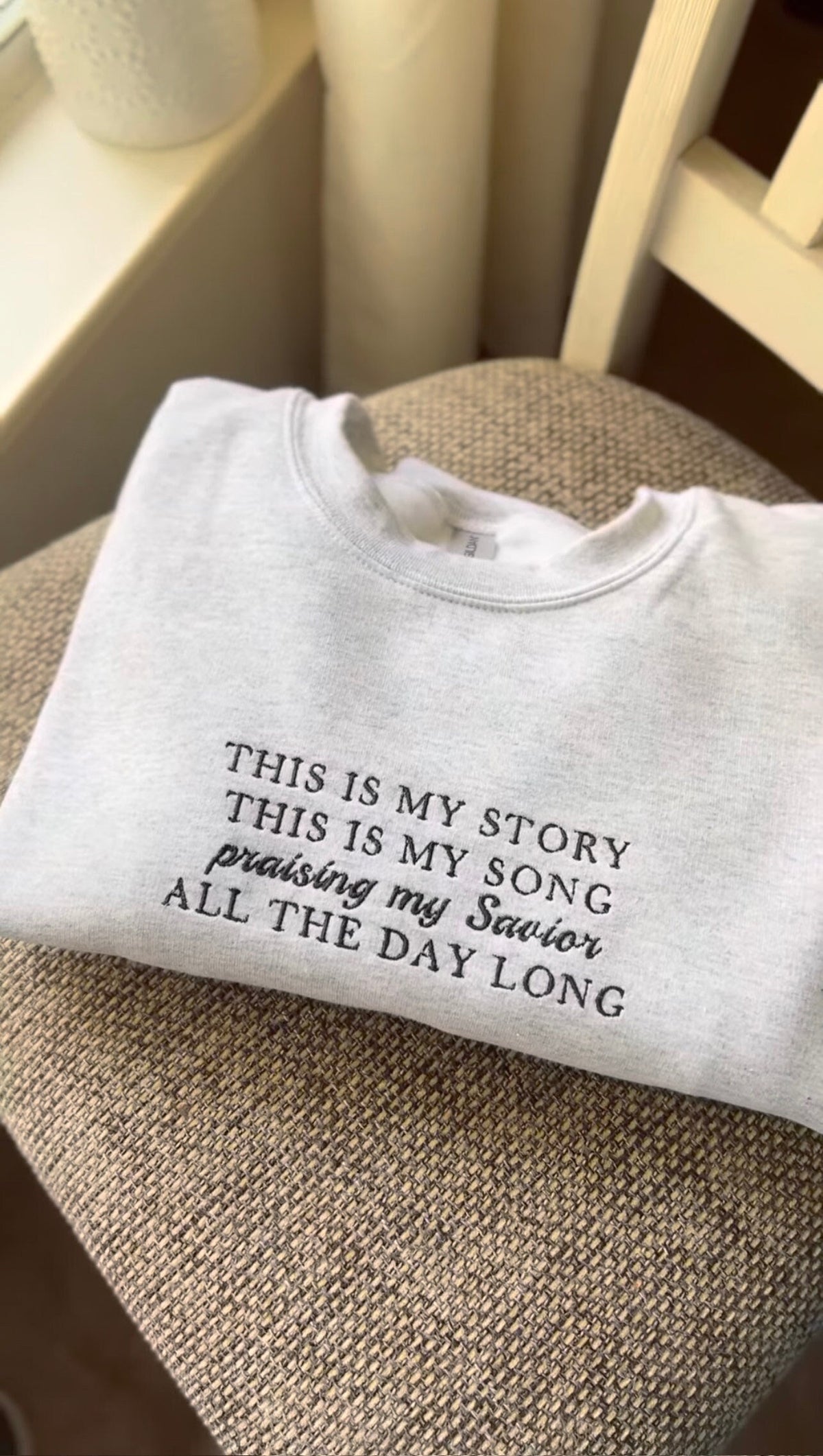 A gray sweatshirt with the text 'This is my story This is my song Praising my Savior All the day long' embroidered on it.
