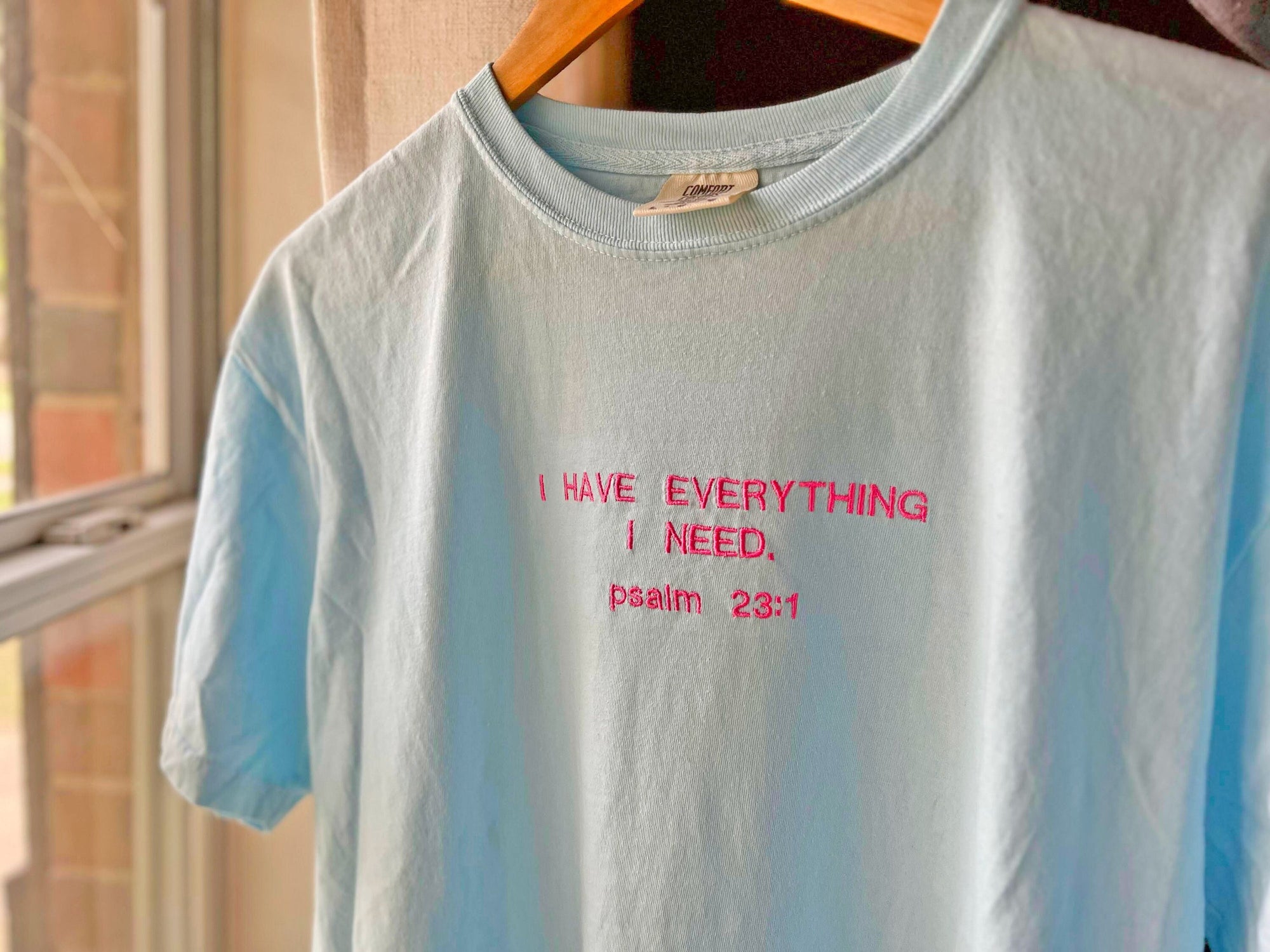 A chambray blue crewneck t-shirt with the embroidered text 'I HAVE EVERYTHING I NEED. psalm 23:1' in red.