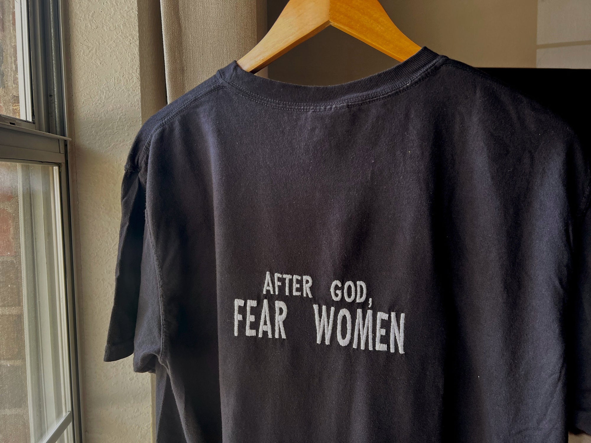 Black t-shirt with the text 'AFTER GOD, FEAR WOMEN' embroidered on the back in white lettering.