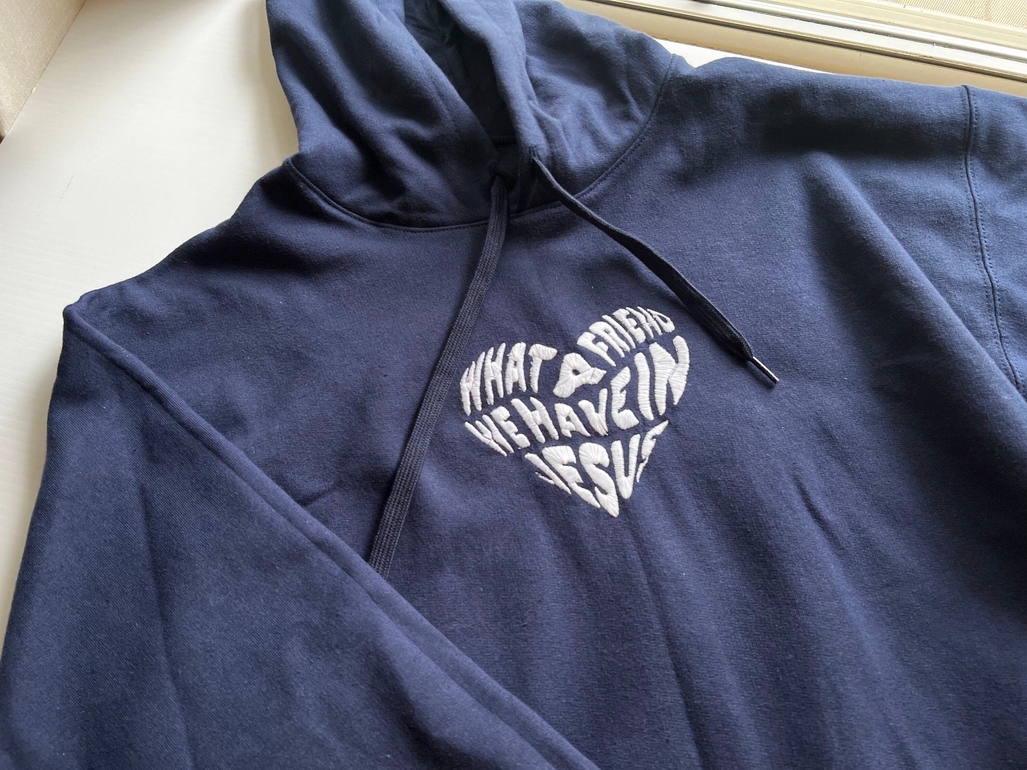 Navy blue hoodie with 'What a Friend We Have in Jesus' embroidered text on the front.
