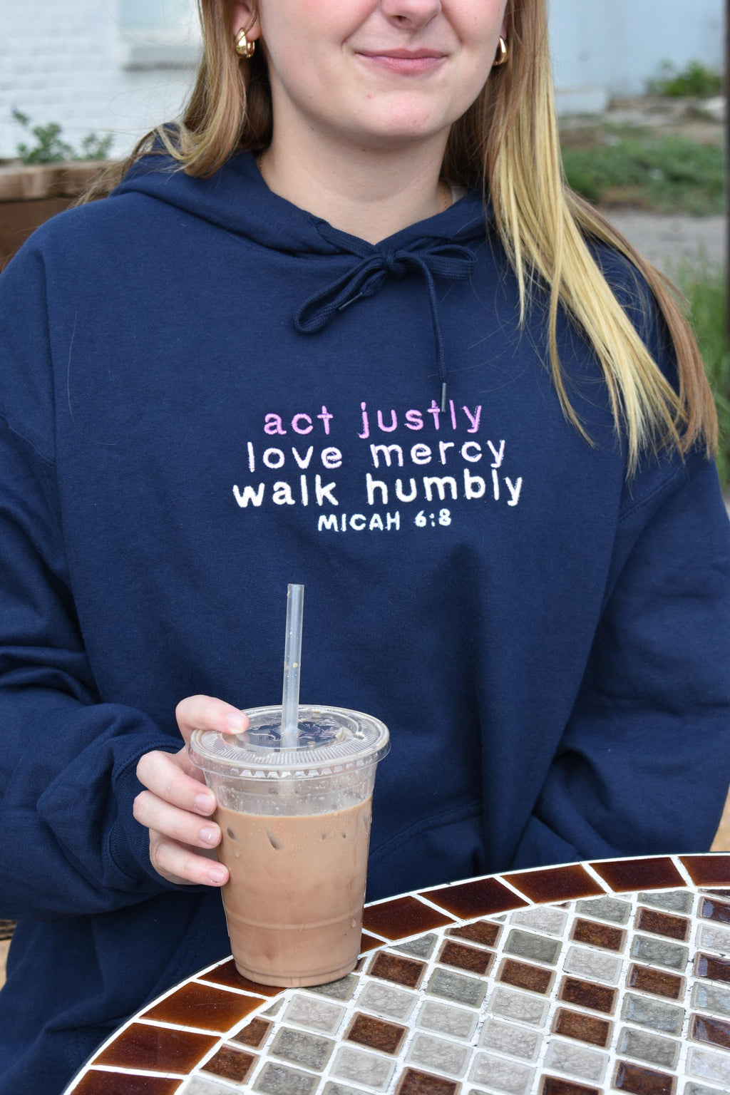 Woman is wearing a navy blue hoodie with embroidered text on the front that reads:

"act justly
love mercy
walk humbly
MICAH 6:8"