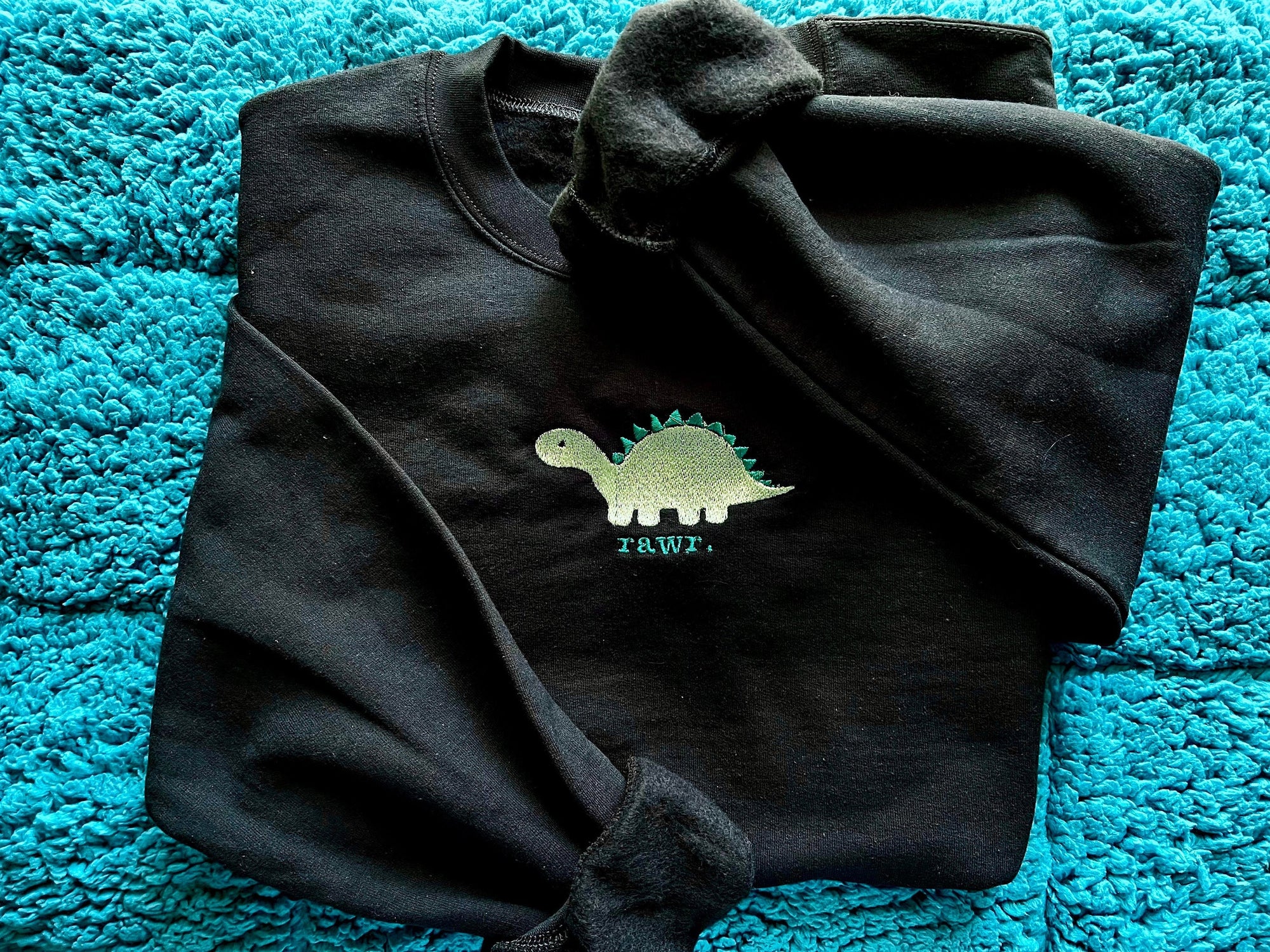 Black sweatshirt with a green dinosaur and text embroidery on the front.