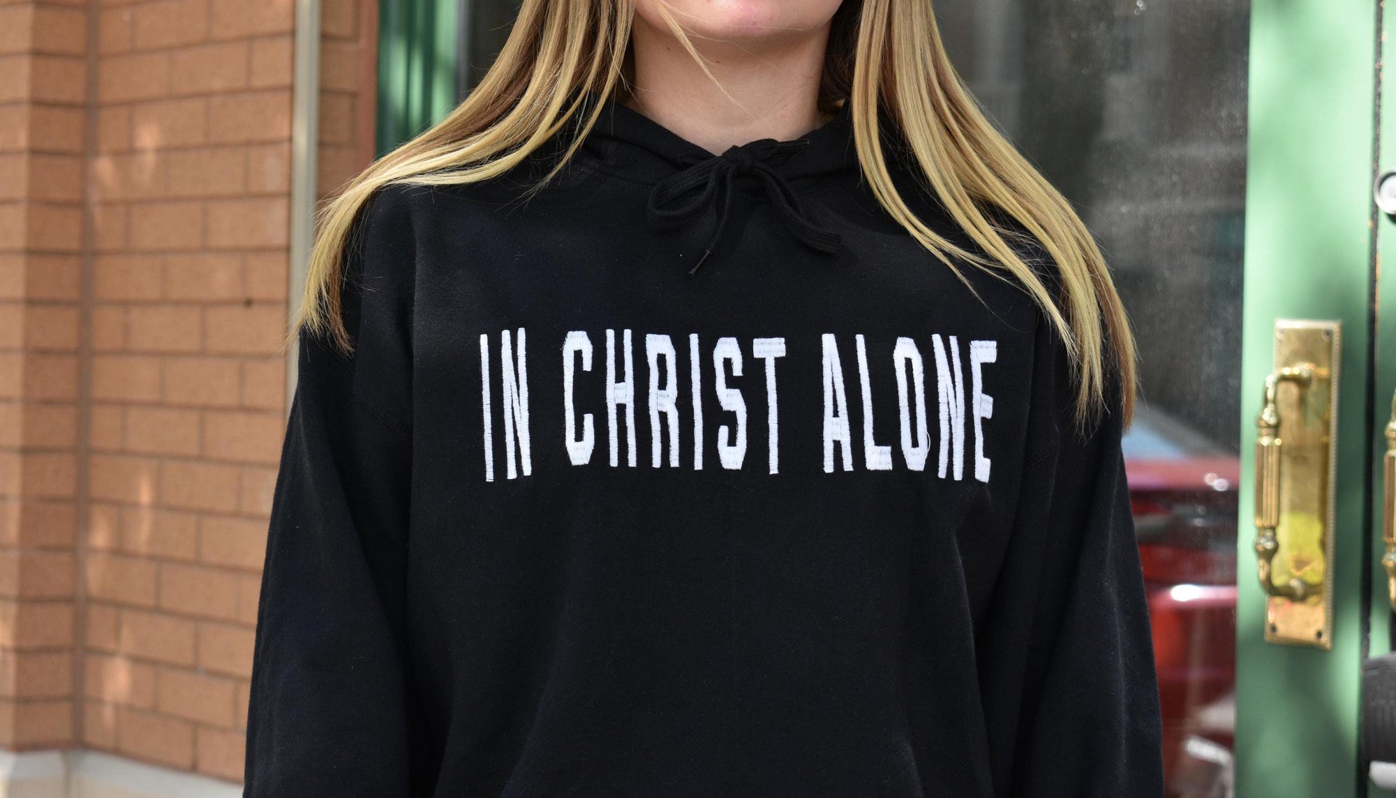 A person wearing a black hoodie with 'IN CHRIST ALONE' embroidered in white on the front.