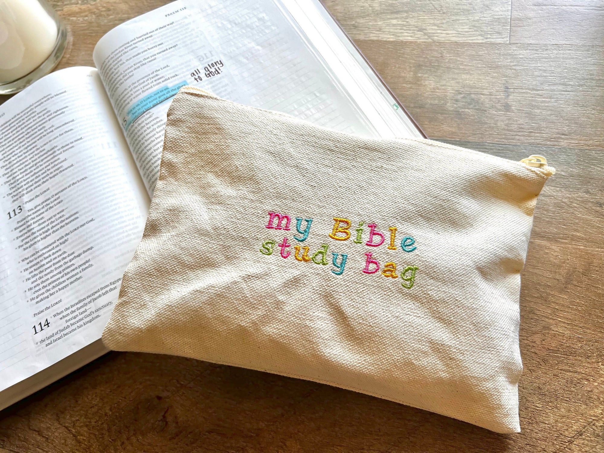 A beige canvas zipper pouch with the text 'my Bible study bag' embroidered in colorful letters on the front, placed on an open Bible.