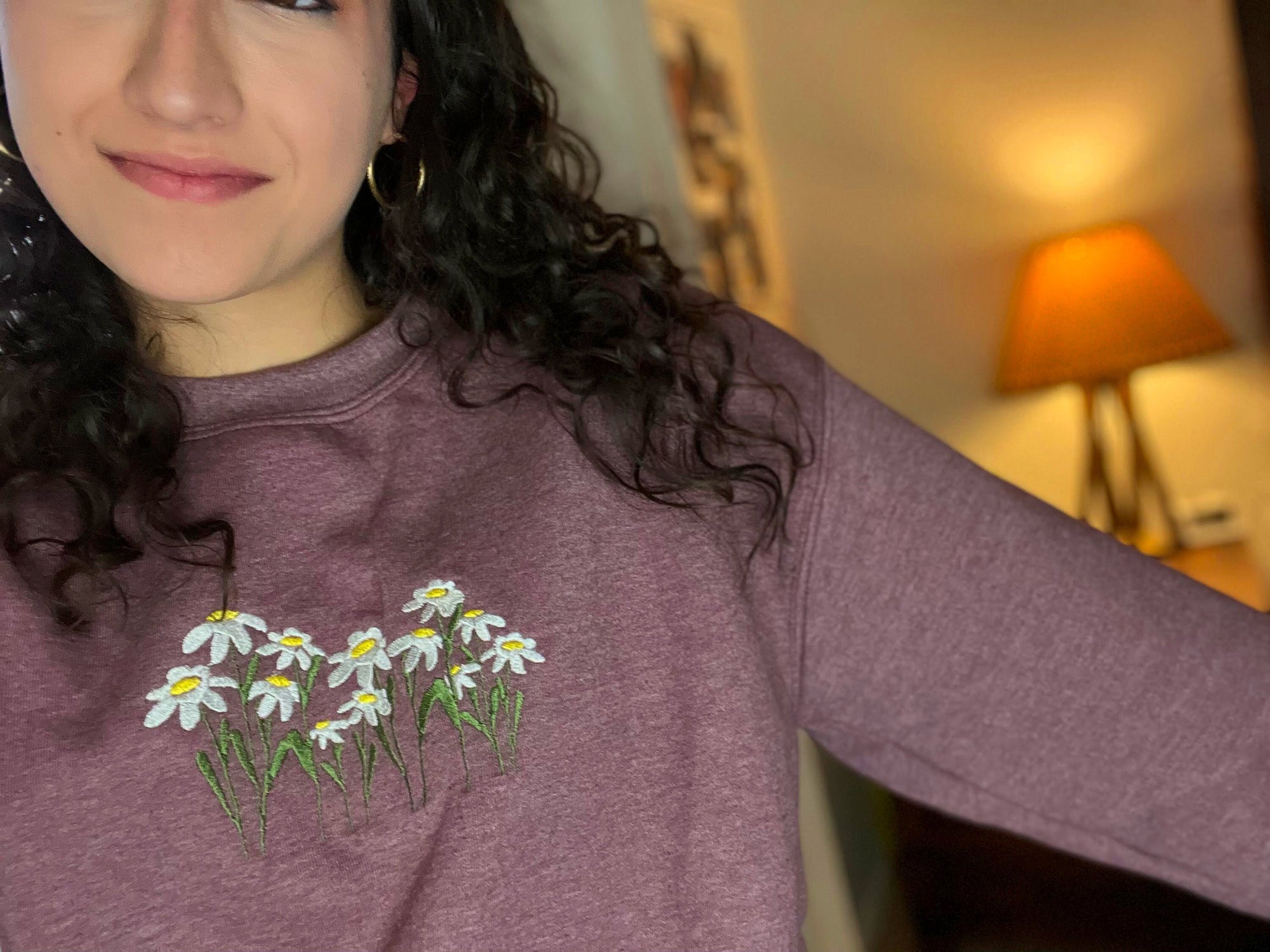 A person wearing a heathered maroon crewneck sweatshirt with a floral embroidered design featuring daisies on the front.